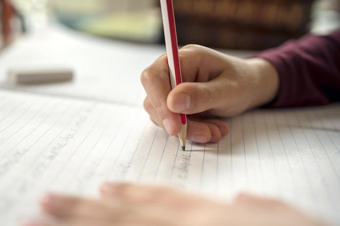 dłoń dziecka piszącego w zeszycie ołówkiem