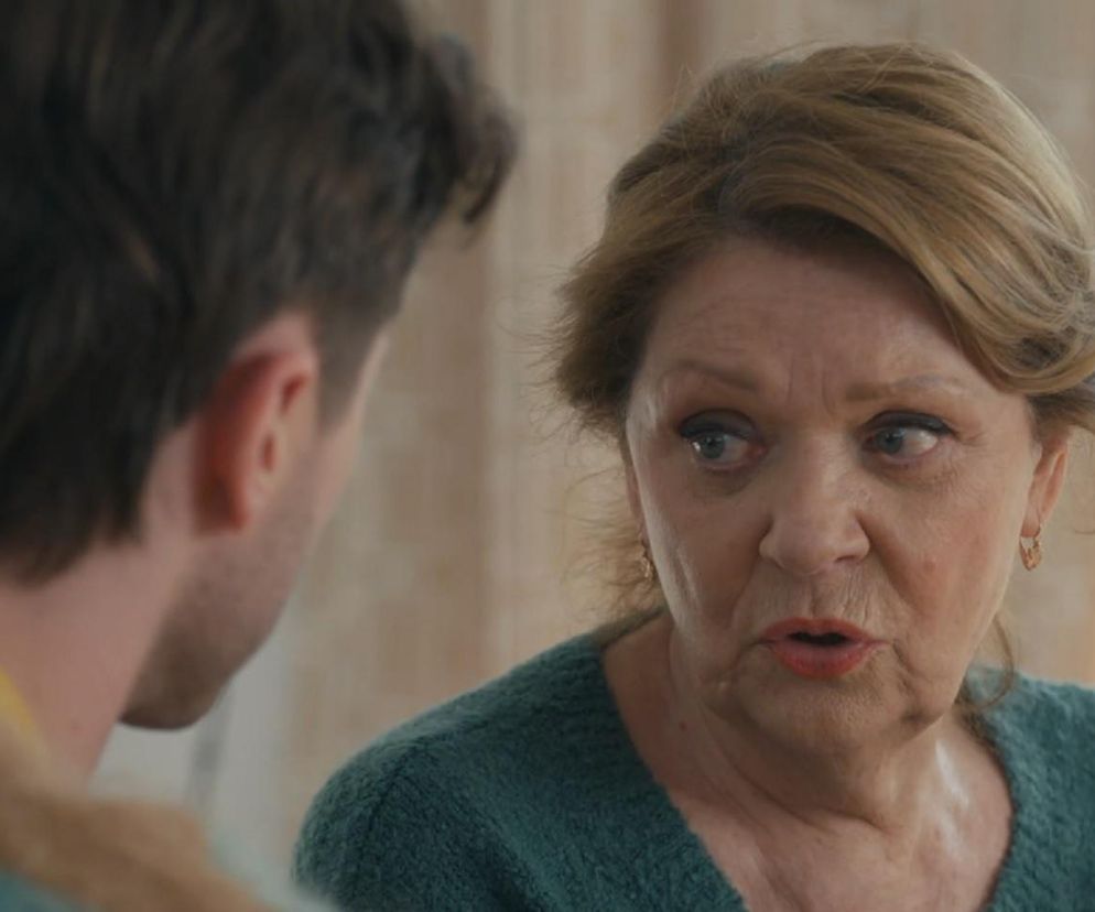 Józefina (Elżbieta Jarosik) z serialu Barwy szczęścia w zielonym swetrze, spoglądająca z niepokojem na Cezarego (Marcel Opaliński), którego widać z tyłu. Scena z odcinka 3251, gdzie omawiają problemy ze spłatą kredytu i przyszłość stadniny. Więcej o dramatycznych losach bohaterów na Super Seriale.