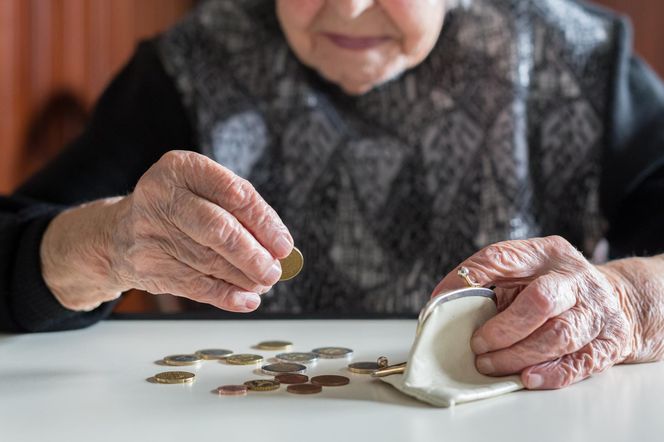 Dłonie starszej osoby liczą monety i wkładają je do portmonetki, co symbolizuje oszczędności i trudności finansowe seniorów. Temat waloryzacji emerytur 2026 i jej niskiego poziomu poruszono na portalu Poradnik Zdrowie.