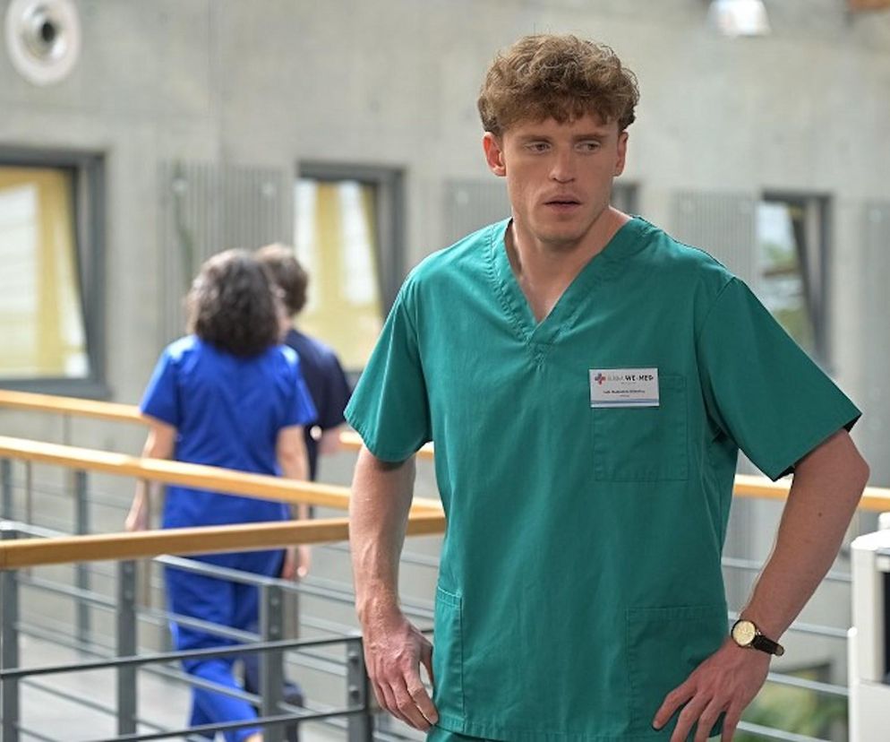 Radek (Karol Biskup) w zielonym stroju medycznym, z przerażeniem na twarzy, stoi w korytarzu kliniki We-Med, gdzie niespodziewana wizyta byłej dziewczyny w 4073 odcinku serialu Pierwsza miłość przyniesie szokujące wieści. Więcej o losach bohaterów przeczytasz na Super Seriale.
