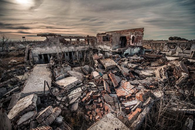 Zrujnowany budynek, z którego pozostały tylko fragmenty ścian i gruzy, pod pochmurnym, ciemnym niebem, symbolizujący zniszczenie wojenne. Scena w opuszczonym miejscu odzwierciedla artykuł o odporności miast na wojnę, o czym możesz przeczytać na Poradnik Zdrowie.
