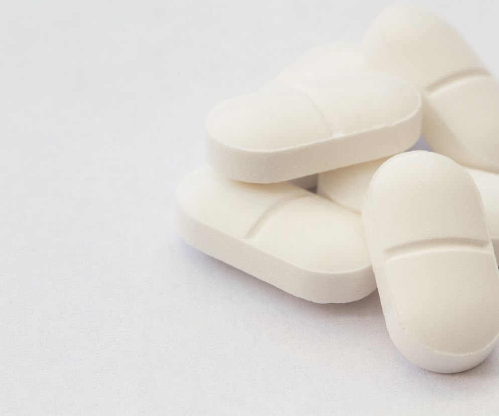 Garść białych tabletek paracetamolu na jasnym tle. Mogą to być tabletki 500 mg, stosowane przeciwbólowo i przeciwgorączkowo. Dowiedz się więcej o dawkowaniu i skutkach ubocznych paracetamolu na Poradnik Zdrowie.