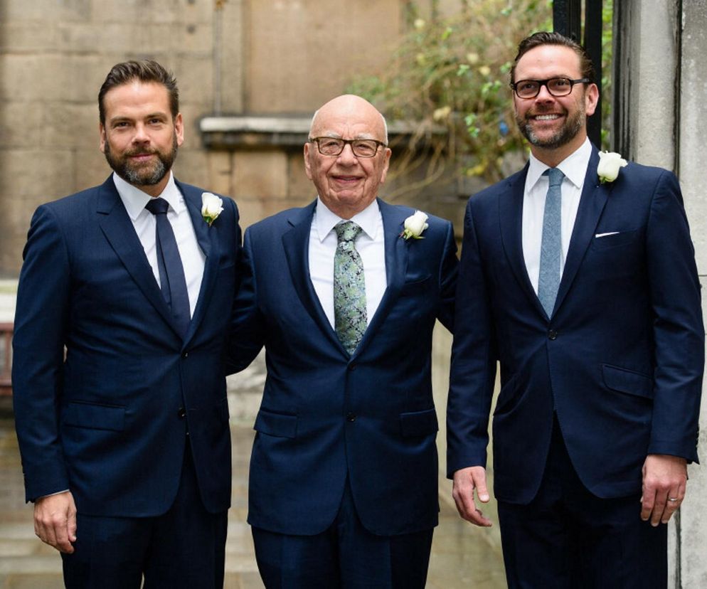 Rupert Murdoch w ciemnym garniturze i krawacie w zielone wzory, uśmiechnięty, stojący między swoimi synami: Lachlanem (z brodą) i Jamesem (w okularach), obaj w granatowych garniturach i krawatach. O kulisach sukcesji imperium Murdochów przeczytasz na Super Biznes.