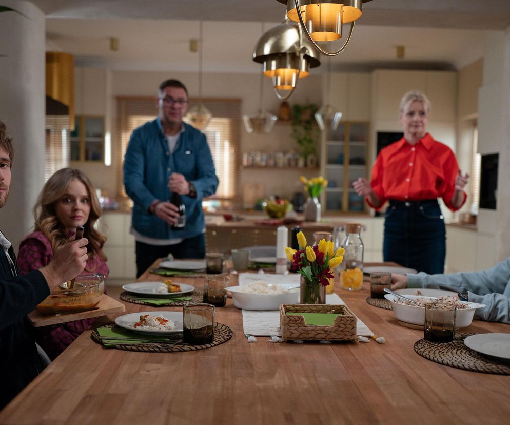 Rodzina Boskich podczas niezręcznego rodzinnego obiadu. Tomasz Karolak i Małgorzata Kożuchowska stoją w kuchni, a Maciej Musiał, Olga Kalicka i Mateusz Pawłowski siedzą przy stole. Artykuł i więcej zdjęć z 295 odcinka Rodzinka.pl znajdziesz na Super Seriale.
