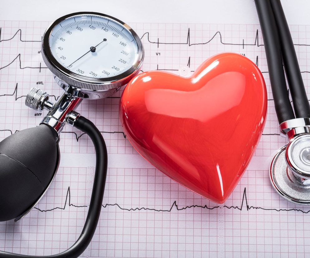 Analogowy ciśnieniomierz z mankietem, stetoskop oraz czerwone, błyszczące serce na tle wydruku EKG. Grafika symbolizuje dbałość o zdrowie serca i kontrolę ciśnienia. Więcej informacji o ciśnieniomierzach nadgarstkowych znajdziesz na Poradnik Zdrowie.