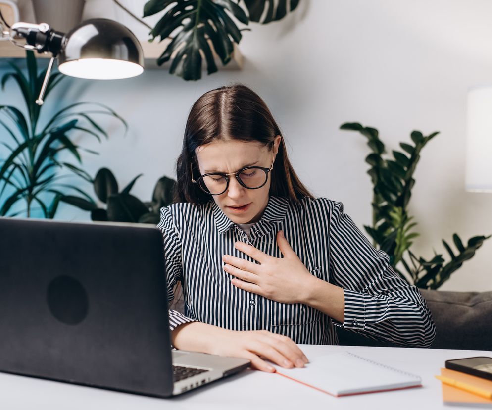 Młoda kobieta pracująca na komputerze, ma trudności w oddychaniu i ból w klatce piersiowej