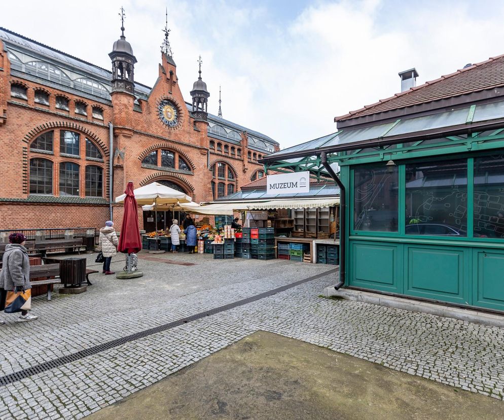 Ceglana elewacja Hali Targowej w Gdańsku z wieżyczkami. Przed nią stragany. O zmianach w obiekcie przeczytasz w Architektura.