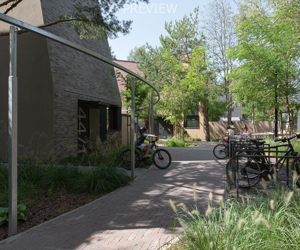 Osiedle Nowy Strzeszyn w Poznaniu, zaprojektowane przez pracownię Insomia, gdzie zabudowę dostosowano do istniejącej zieleni. Widoczna ścieżka z kostki brukowej, dzieci na rowerach oraz stojaki rowerowe, podkreślające wspólnotowy charakter przestrzeni, o której przeczytasz więcej na Architektura Murator Plus.