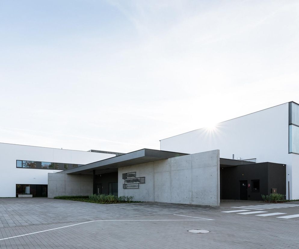 Nowoczesny budynek Szkoły Podstawowej w Cerekwicy, projektu LAB 3 Architekci Sp. z o. o., z wejściem podkreślonym betonowymi elementami i zadaszeniem. Obiekt wyróżnia się prostotą formy i harmonijnym wkomponowaniem w krajobraz, o czym przeczytasz na Architektura Murator Plus.