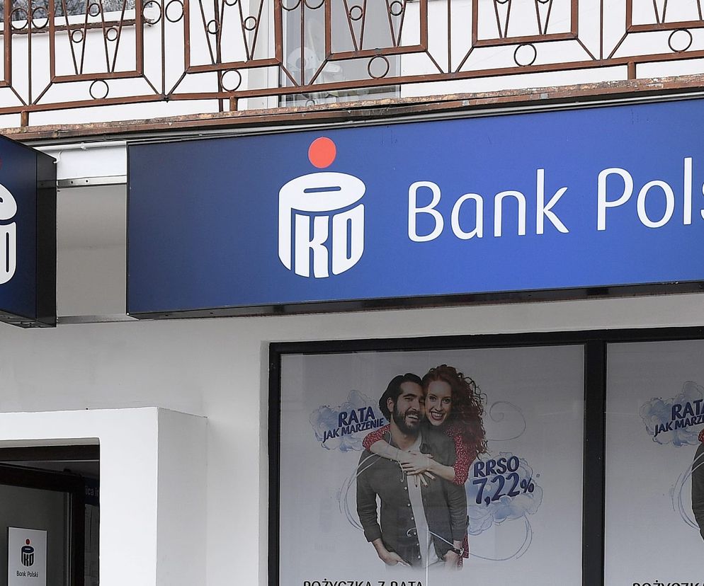 Logo PKO Bank Polski w kolorze niebieskim na elewacji budynku, pod nim witryna z reklamą kredytu Rata jak marzenie z uśmiechniętą parą. Informacje o przerwach technicznych w bankowości znajdziesz na Super Biznes.