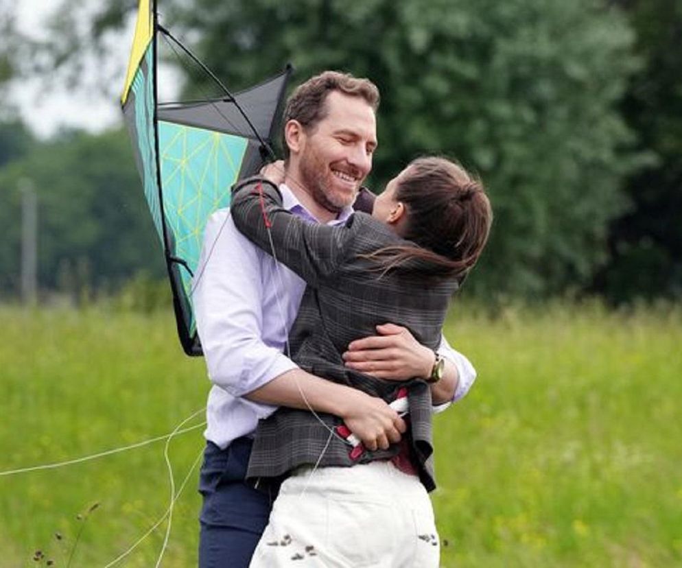 Aktorzy Robert Gulaczyk jako Szczepan i Marta Juras jako Gabrysia z serialu Barwy szczęścia obejmują się na zielonej łące, obok nich kolorowy latawiec. Scena przedstawia romantyczne wagary i beztroskie chwile, o których można przeczytać na Super Seriale.