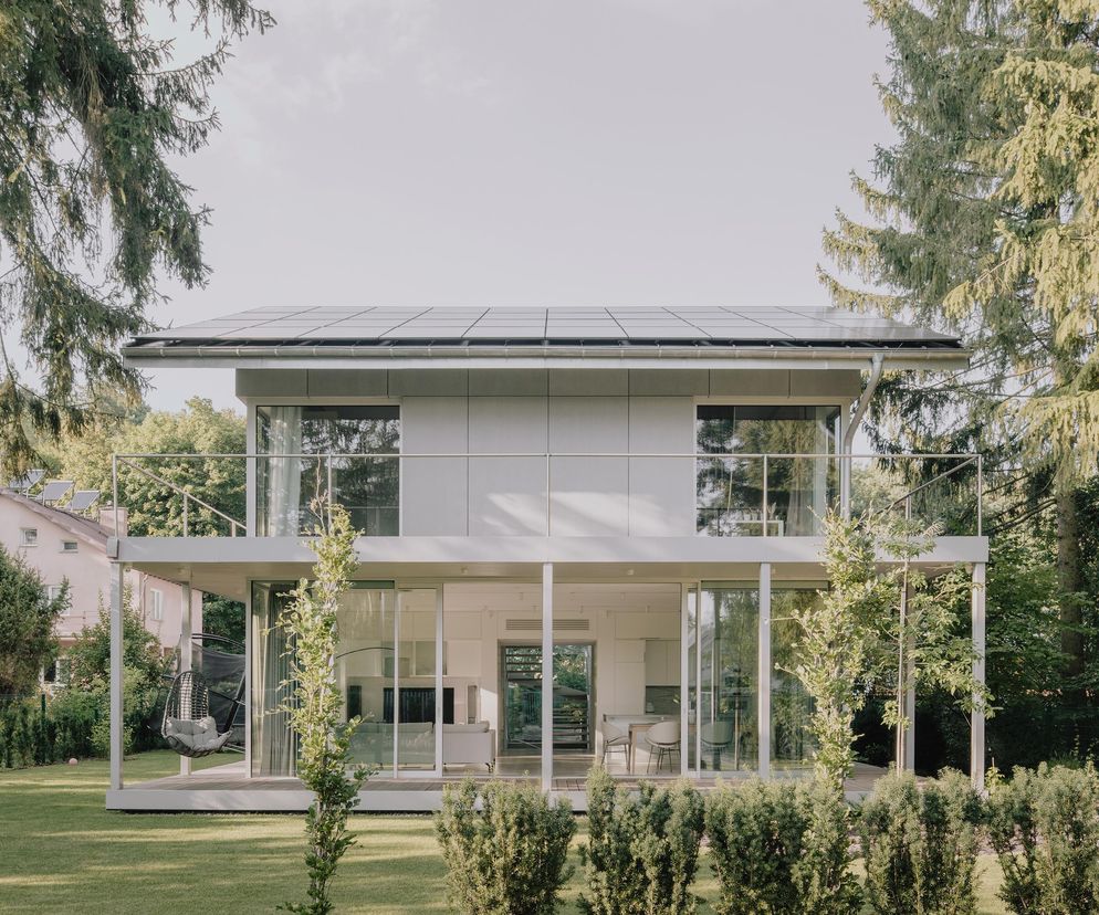 Nowoczesny dom jednorodzinny BDR Architekci w Konstancinie-Jeziornej, z dużymi przeszkleniami i panelami fotowoltaicznymi na dachu, otoczony zielenią. Projekt promuje zrównoważoną Architektura Murator Plus.