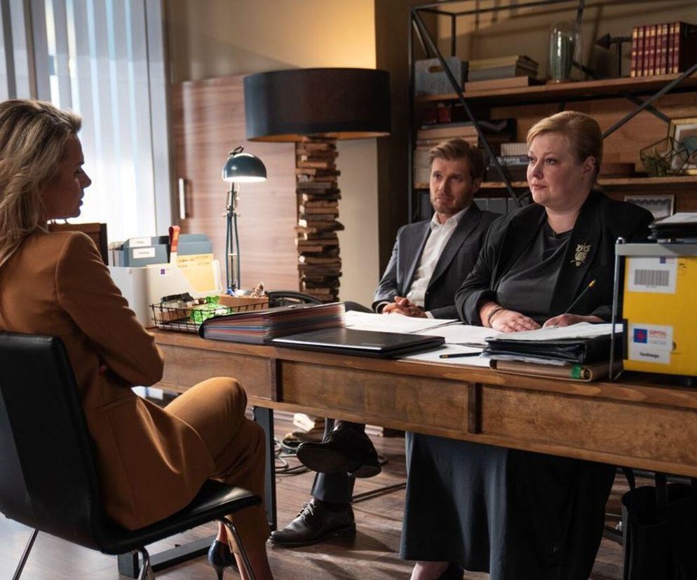 Trzy osoby, w tym Agata Woźnicka (Emilia Komarnicka) w brązowym garniturze, Tomasz Ciachorowski jako Maks Beger i Katarzyna Cynke grająca Elżbietę Czajkowską, siedzą przy stole podczas spotkania w gabinecie. Beger i Czajkowska, kontrolerzy z Ministerstwa Zdrowia, przyglądają się Woźnickiej. Więcej o ich działaniach znajdziesz na stronie Super Seriale.