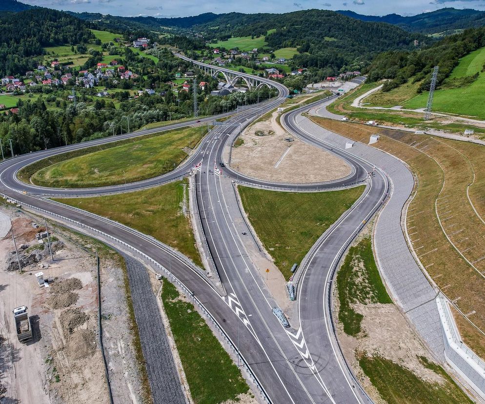 Nowy odcinek drogi ekspresowej S1 w rejonie Przybędzy, z widocznymi węzłami i estakadą nad doliną, otoczony zielonymi wzgórzami. Inwestycja znacząco usprawni ruch, o czym można przeczytać na portalu Super Biznes.