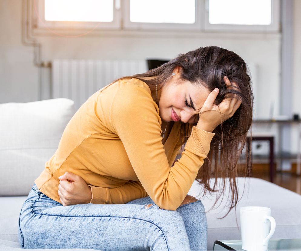 Kobieta siedzi na kanapie i trzyma się za obolały brzuch