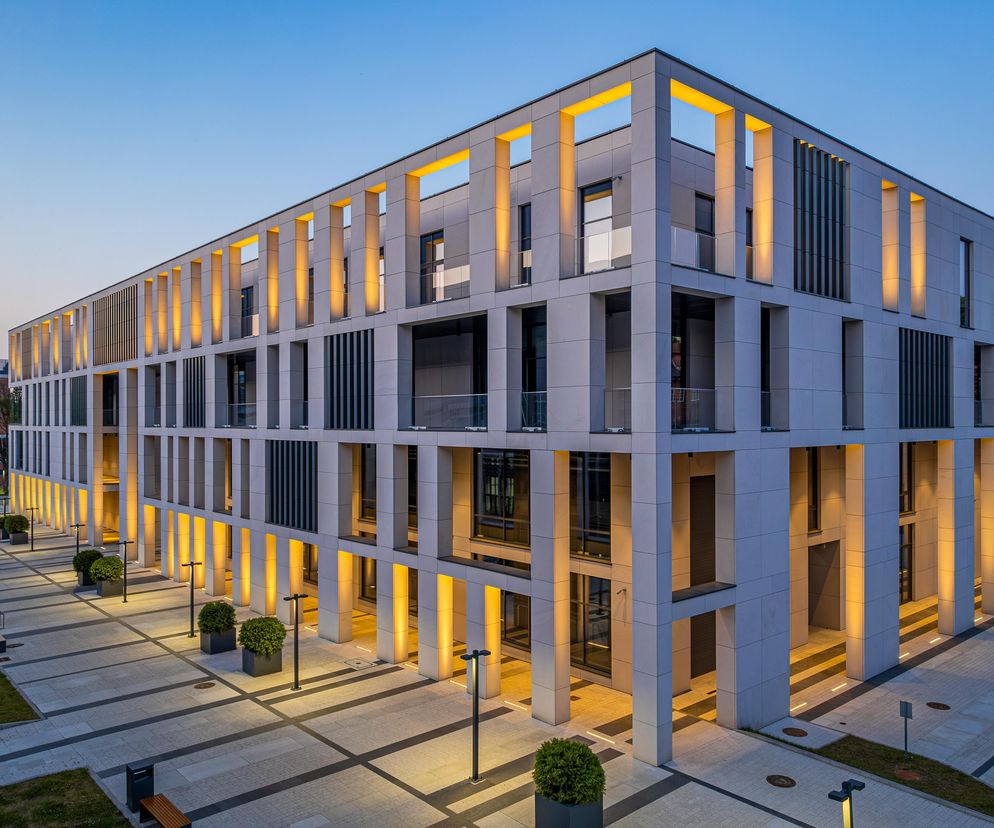 Nowoczesny budynek Centrum Ekoinnowacji Politechniki Gdańskiej autorstwa FORT Taraszkiewicz Architekci Sp. z o.o., z fasadą w jasnych odcieniach, podkreślony pionowymi słupami z ciepłym oświetleniem. Nocne zdjęcie podkreśla proekologiczne rozwiązania tej realizacji zgłoszonej do konkursu Życie w Architekturze, o czym można przeczytać na Architektura Murator Plus.