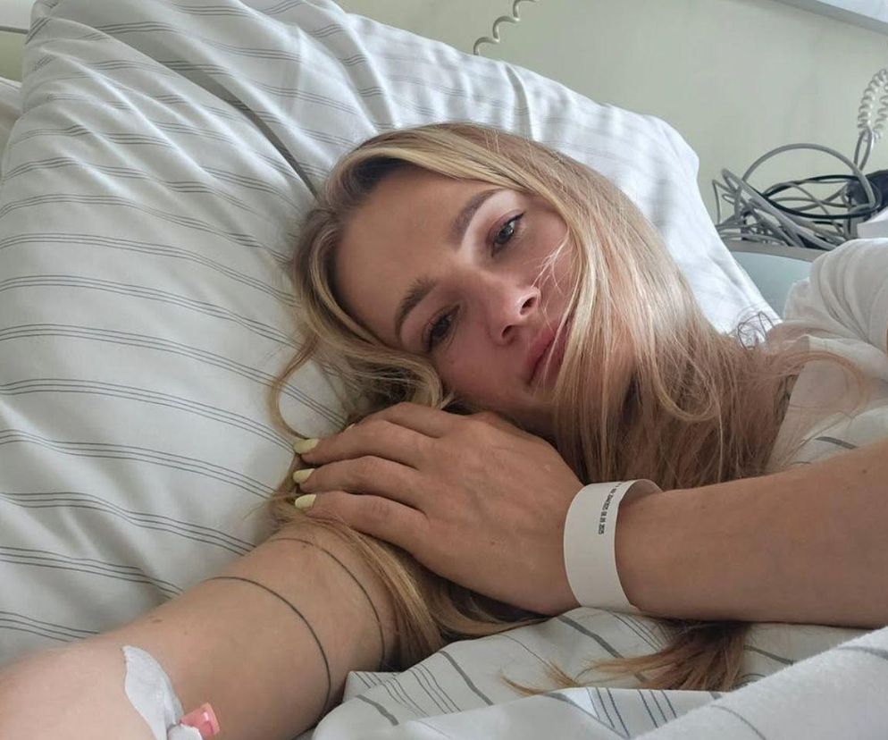 Polska szablistka Angelika Wątor leżąca w łóżku szpitalnym po poważnej operacji, z widocznym wenflonem na ręce i szpitalną opaską. Jej wzrok skierowany jest w stronę obiektywu, a twarz wyraża zmęczenie. Więcej o jej walce o zdrowie przeczytasz na Poradnik Zdrowie.