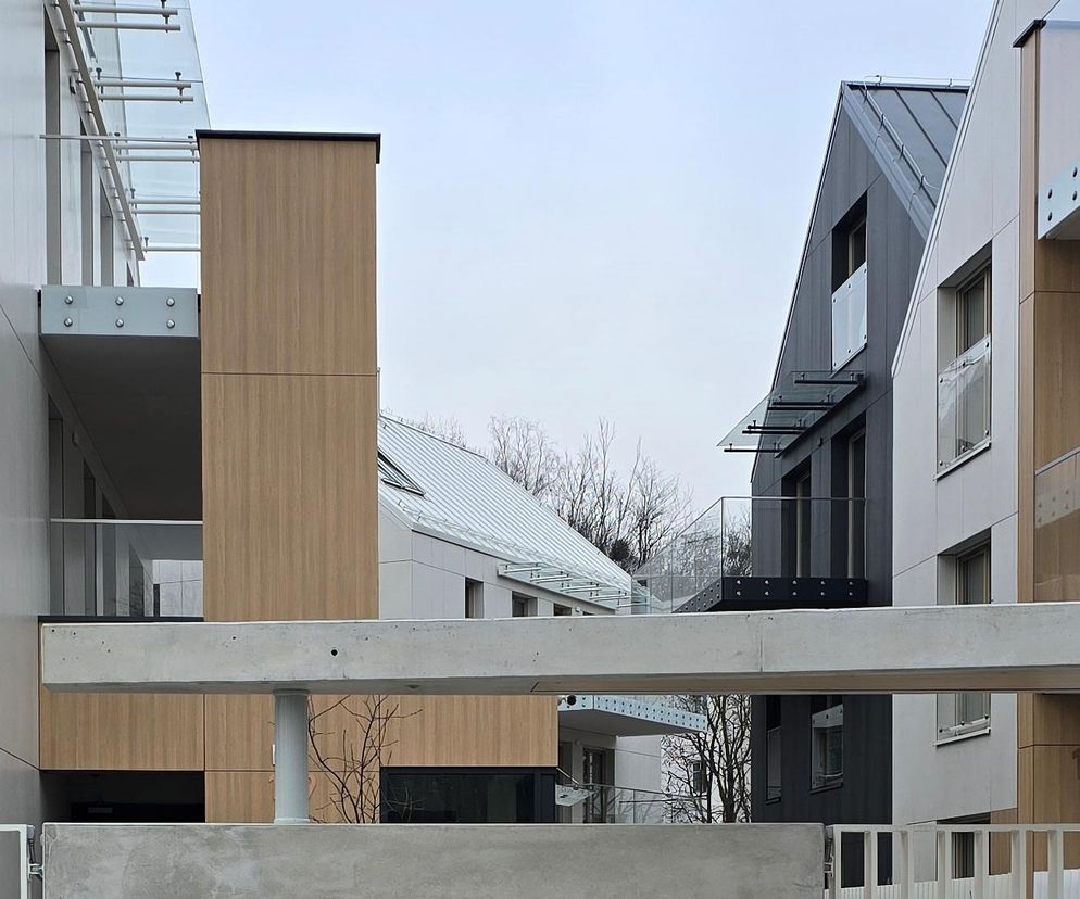 Elegancki zespół budynków wielorodzinnych Supernova w Gdyni z białymi i ciemnoszarymi elewacjami, nawiązującymi do sąsiedniej zabudowy. Widoczne białe balustrady balkonów, drewniane panele ścienne oraz okna połaciowe, co stanowi istotny projekt architektoniczny opisywany na Architektura Murator Plus.