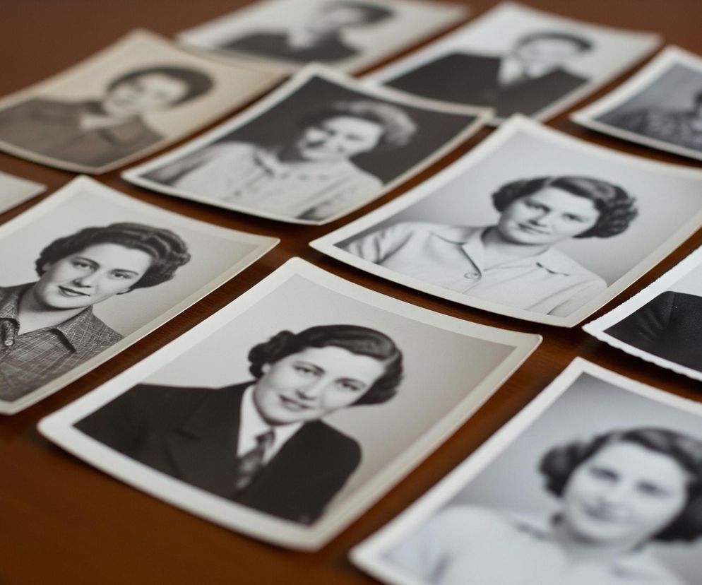 Na brązowym, drewnianym blacie leży rozłożonych kilkanaście czarno-białych fotografii portretowych. Większość zdjęć przedstawia młode kobiety z fryzurami i ubiorem typowym dla połowy XX wieku, często uśmiechnięte i patrzące prosto w obiektyw. Kilka zdjęć przedstawia mężczyzn w garniturach i krawatach, również uśmiechniętych. Fotografie są częściowo nałożone na siebie, tworząc nieregularny układ, a niektóre z nich są lekko rozmazane, szczególnie te w tle.