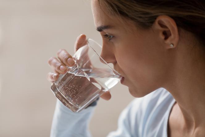 Zbliżenie na profil kobiety, która pije wodę ze szklanki. 
