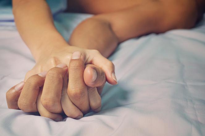 Mężczyzna trzyma kobietę za rękę w łóżku