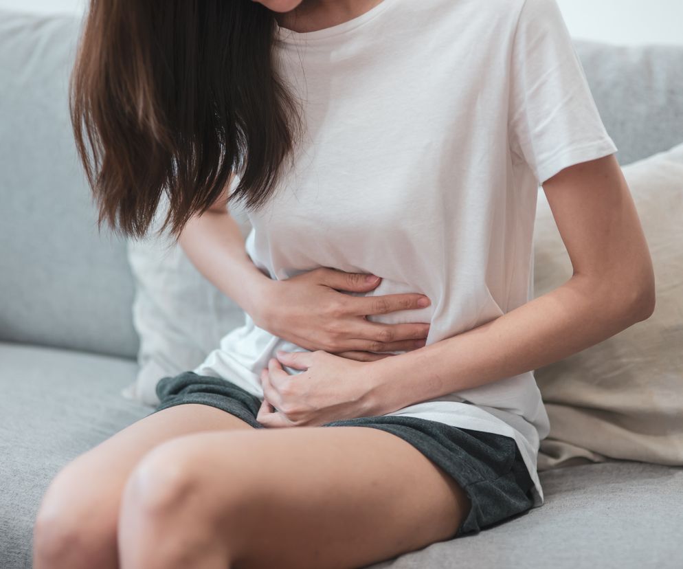 Kobieta trzyma się za brzuch, siedzi na kanapie.