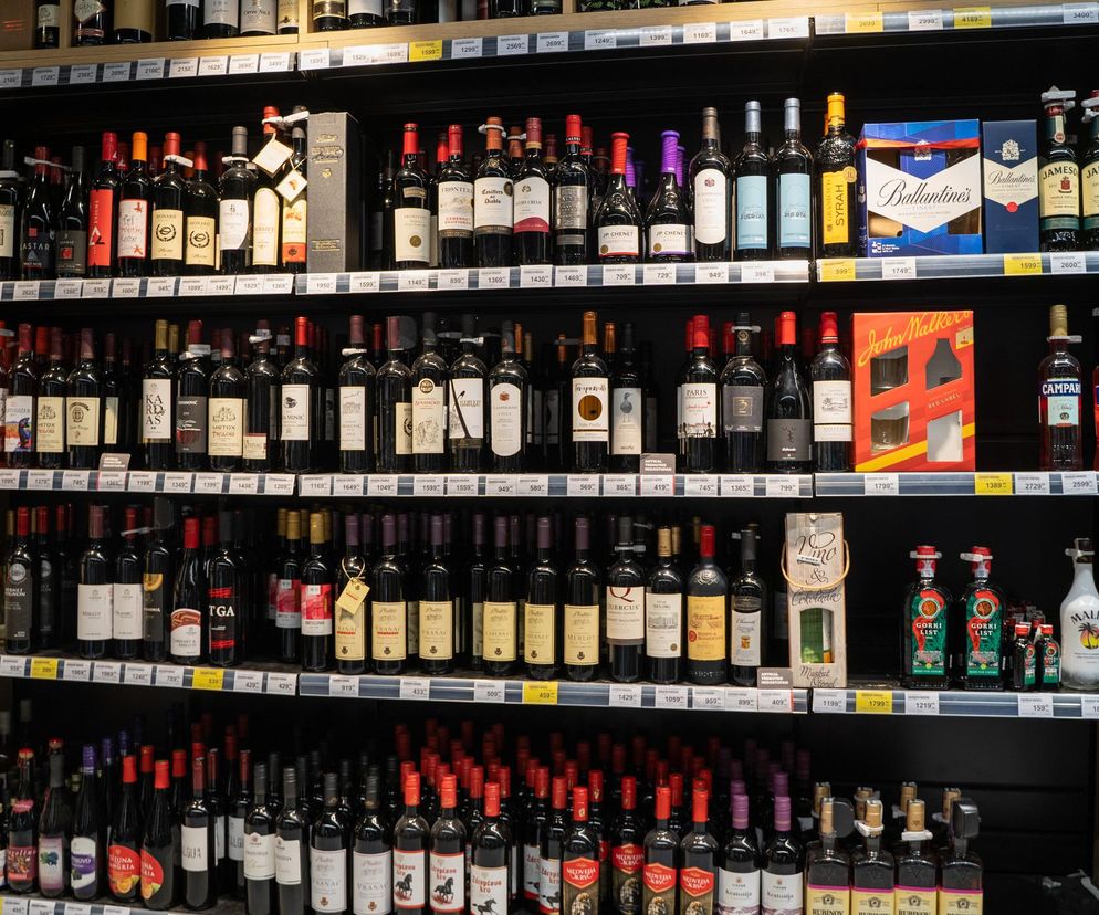 Duży regał w sklepie, na którym widać liczne butelki z różnymi rodzajami alkoholu, w tym wina, whisky, wódki oraz likiery, ułożone w rzędach, z widocznymi cenami. Ta wizualizacja dostępności alkoholu podkreśla apel lekarzy o nocną prohibicję, o czym przeczytasz na Poradnik Zdrowie.