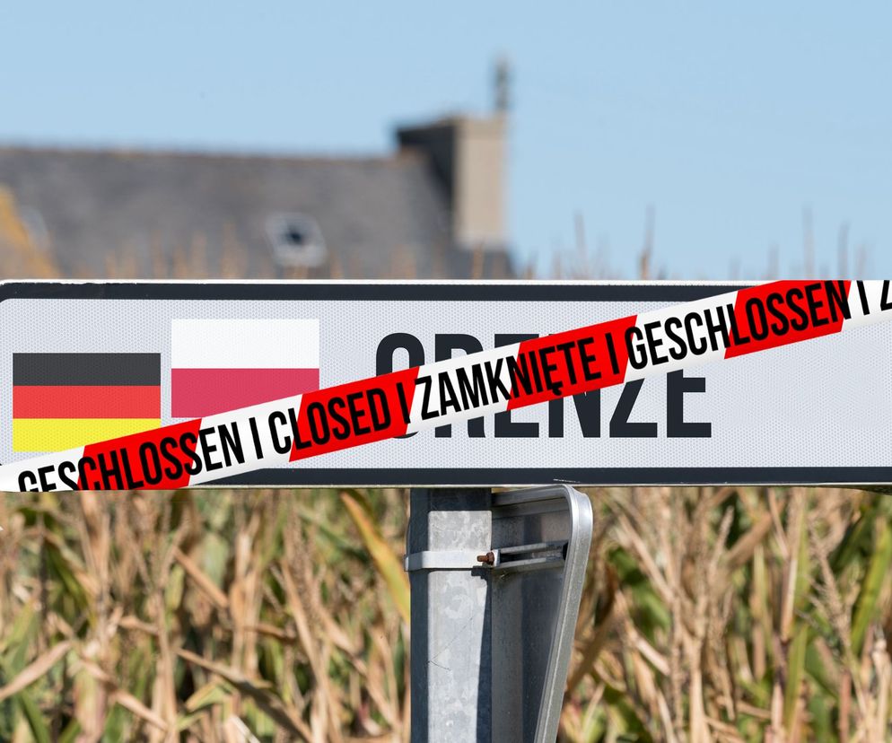Tablica informacyjna z flagami Polski i Niemiec, na której widnieje napis „GRANICA” przekreślony czerwoną taśmą z napisami „CLOSED” i „ZAMKNIĘTE”. W tle niewyraźne pola uprawne i budynki. Zdjęcie ilustruje temat otwarcia granic, o którym przeczytasz na Poradnik Zdrowie.