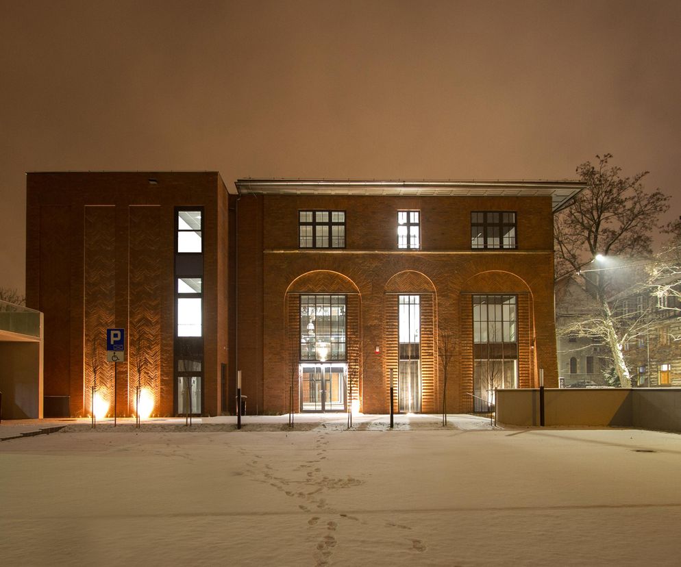 Zrewitalizowany budynek dawnej gazowni w Zabrzu, obecnie Centrum Usług Społecznych, oświetlony w nocy, z widocznym śniegiem na dziedzińcu. Architektura ceglana z nowoczesnymi przeszkleniami. Projekt Plus Architekci Sp. z o.o., nominowany w konkursie Życie w Architekturze 2025, o którym przeczytasz na Architektura Murator Plus.