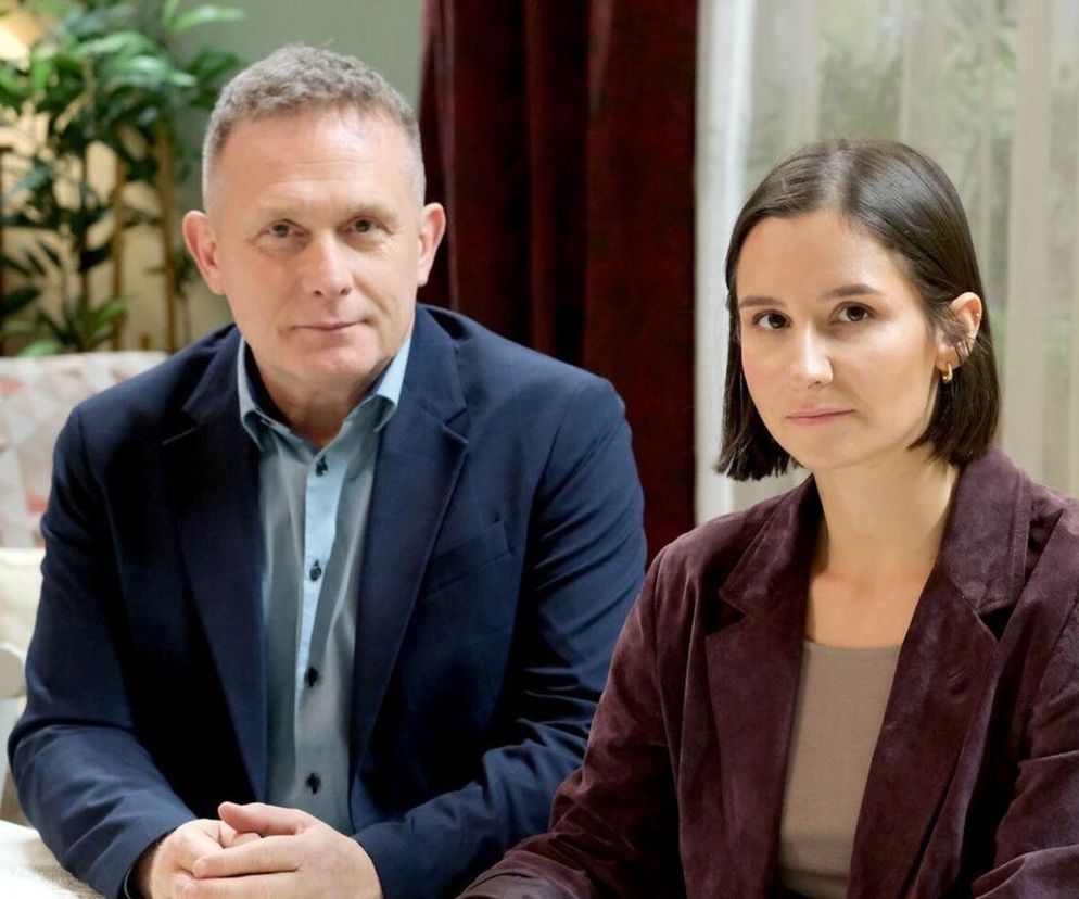 Aktor Robert Moskwa jako Artur Rogowski i aktorka Amanda Mincewicz jako Agnes, siedzą obok siebie, patrząc wprost na widza. Mężczyzna w granatowej marynarce i błękitnej koszuli, kobieta w ciemnobordowej marynarce. Więcej informacji o serialu znajdziesz na Super Seriale.