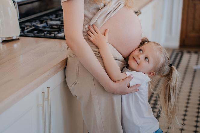 Dziewczynka przytulająca się do ciążowego brzucha mamy