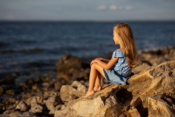 dziewczynka siedząca na skałach nad brzegiem morza