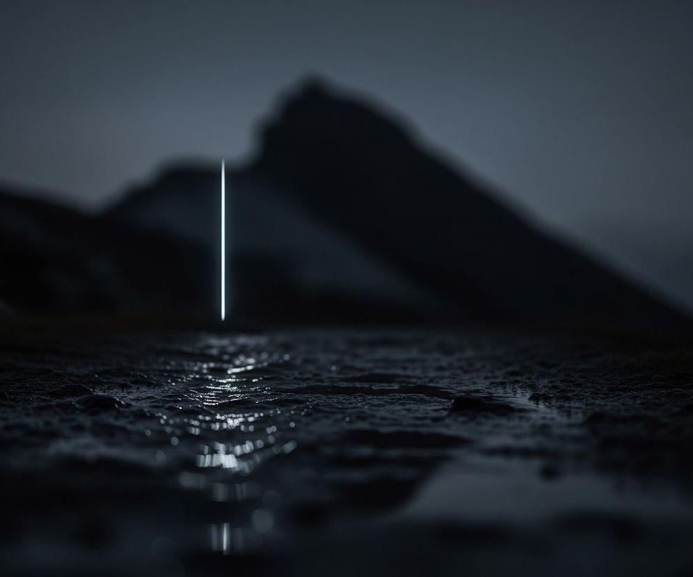 W centrum obrazu znajduje się pionowa, wąska, jasno świecąca linia w kolorze biało-błękitnym, odbijająca się w ciemnej, nieregularnej powierzchni poniżej. Powierzchnia ta, przypominająca mokrą ziemię lub kamienie, jest ciemna i ma liczne refleksy świetlne od linii, rozciągające się w głąb obrazu. Tło stanowią ciemne, niewyraźne zarysy gór lub wzniesień, dominujące po lewej i prawej stronie, w odcieniach szarości i czerni, przechodzące w ciemne, zasnute niebo. Całość utrzymana jest w chłodnej, monochromatycznej palecie barw.