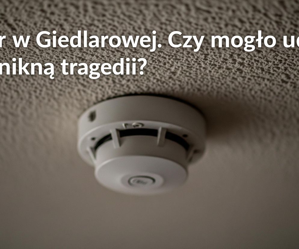 Na suficie z widoczną fakturą typu baranek zamocowany jest biały, okrągły czujnik dymu. Górna część obrazu, na której widnieje tekst, jest ciemniejsza. Biały tekst o treści Pożar w Giedlarowej. Czy mogło udał się uniknąć tragedii? jest umieszczony w lewej górnej części zdjęcia.
