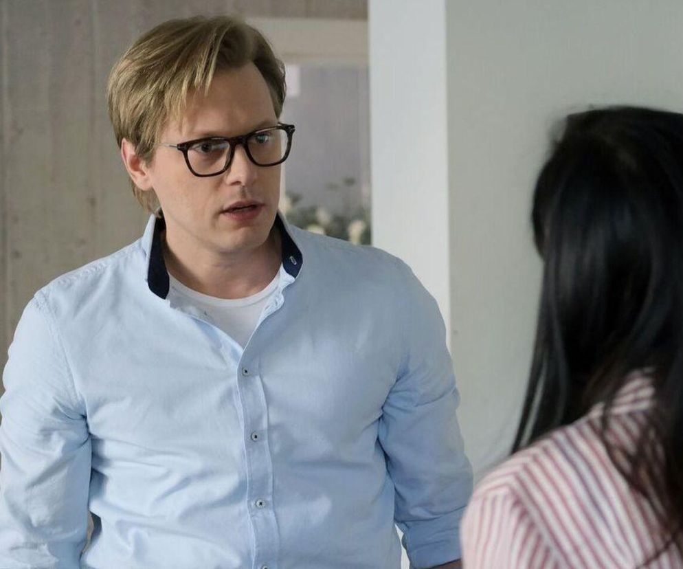 Młody mężczyzna, Radek (Philippe Tłokiński), w okularach i błękitnej koszuli z białym t-shirtem pod spodem, rozmawia z kobietą w pasiastym ubraniu. Scena z serialu M jak miłość przedstawiająca rozwodową wojnę Izy i Radka. O konflikcie tych postaci możesz przeczytać na Super Seriale.