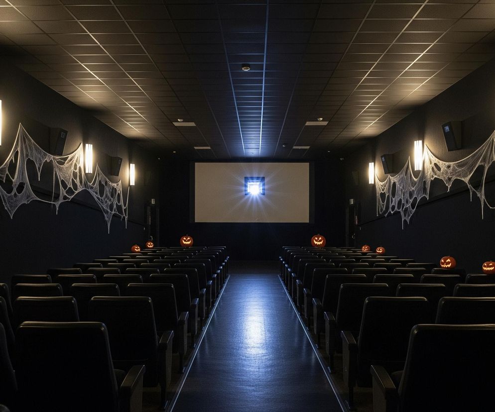 Widoczna jest pusta sala kinowa utrzymana w ciemnych kolorach, z czarnymi ścianami i sufitem. Po obu stronach sali, na wysokości górnej części ścian, rozwieszone są duże, białe pajęczyny, a między nimi rozmieszczono pionowe, podłużne lampy emitujące ciepłe, żółte światło. Na ekranie w centralnej części ściany frontowej wyświetlany jest jasny obraz z niebieskawą poświatą. Wśród rzędów czarnych foteli, na ich oparciach, równomiernie rozłożono kilka pomarańczowych, rzeźbionych dyń, z których każda świeci delikatnym, żółtawym blaskiem.