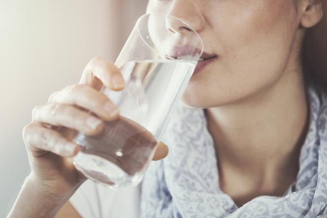 Młoda kobieta pije wodę niegazowaną ze szklanki 