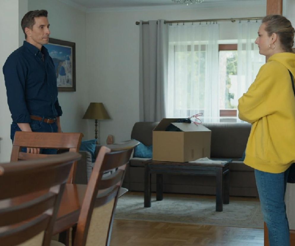 Tomasz (Jakub Sokołowski) i Grażyna (Kinga Suchan) w scenie z serialu Barwy szczęścia, stojący w pokoju z meblami, stołem, kanapą i pudłem na środku. Relacja Tomasza i Grażyny się popsuje, o czym można przeczytać na Super Seriale.
