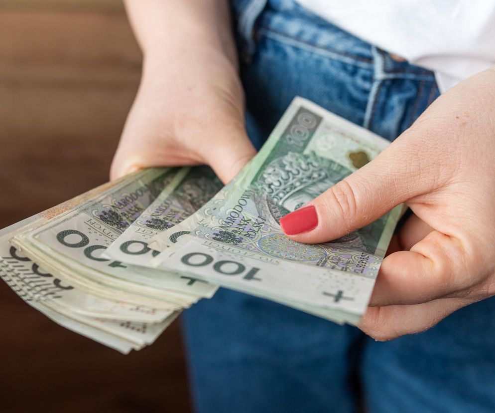 Kobieca dłoń trzyma kilka polskich banknotów stuzłotowych.  Ilustracja do artykułu na Super Biznes o realnych zarobkach Polaków – mediana vs. średnia krajowa.  Dane GUS pokazują dużą rozbieżność między oficjalną średnią a rzeczywistymi dochodami.  Dowiedz się więcej na Super Biznes!