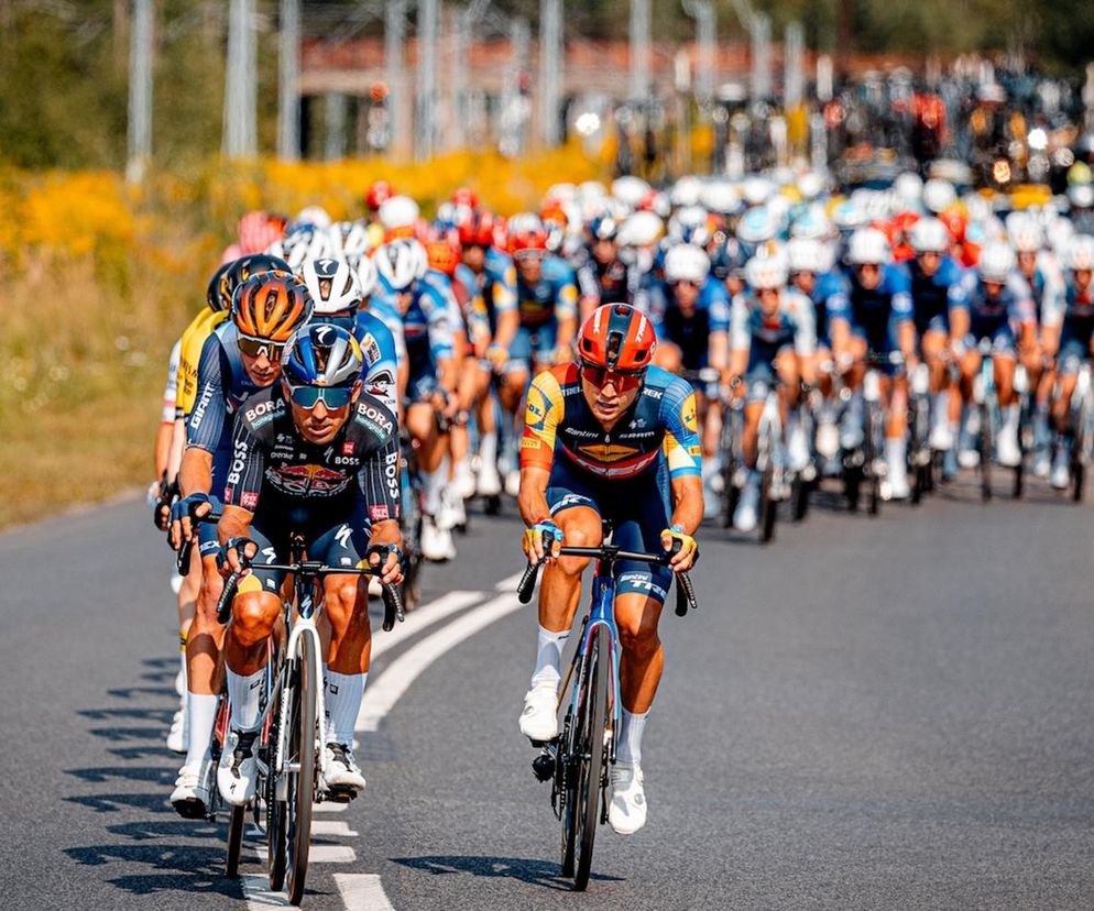 Duża grupa kolarzy jadąca po asfalcie podczas wyścigu Tour de Pologne. O szczegółach sportowych zmagań przeczytasz na SE.