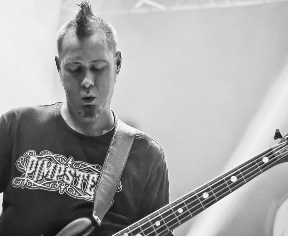 Sam Rivers, basista Limp Bizkit, z charakterystycznym irokezem i bródką, grający na gitarze basowej z zamkniętymi oczami. Zdjęcie w czerni i bieli oddaje emocje muzyka podczas występu. Więcej o chorobie wątroby i przeszczepie przeczytasz na Poradnik Zdrowie.