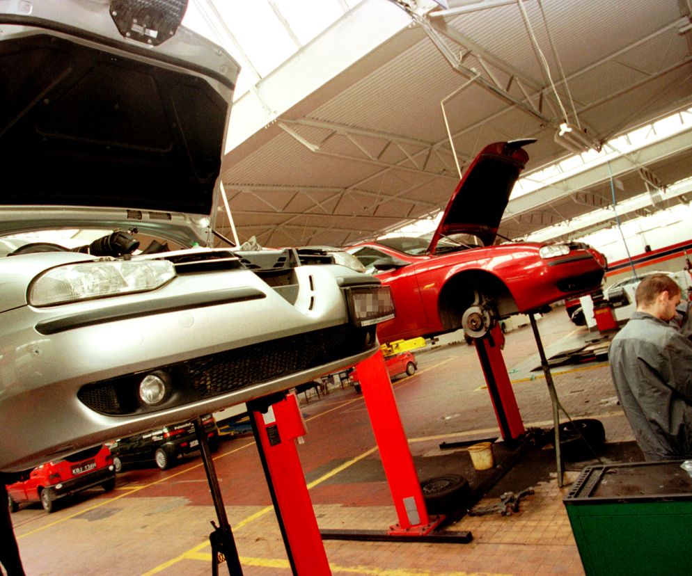 Dwa samochody osobowe na podnośnikach w stacji kontroli pojazdów, gdzie mechanicy przeprowadzają przeglądy techniczne. Scena nawiązuje do planowanych podwyżek opłat za badania techniczne od września 2025 r., o których można przeczytać na portalu Super Biznes. Srebrny samochód z otwartą maską na pierwszym planie, obok czerwone auto również z otwartą klapą silnika, czekające na diagnostykę.
