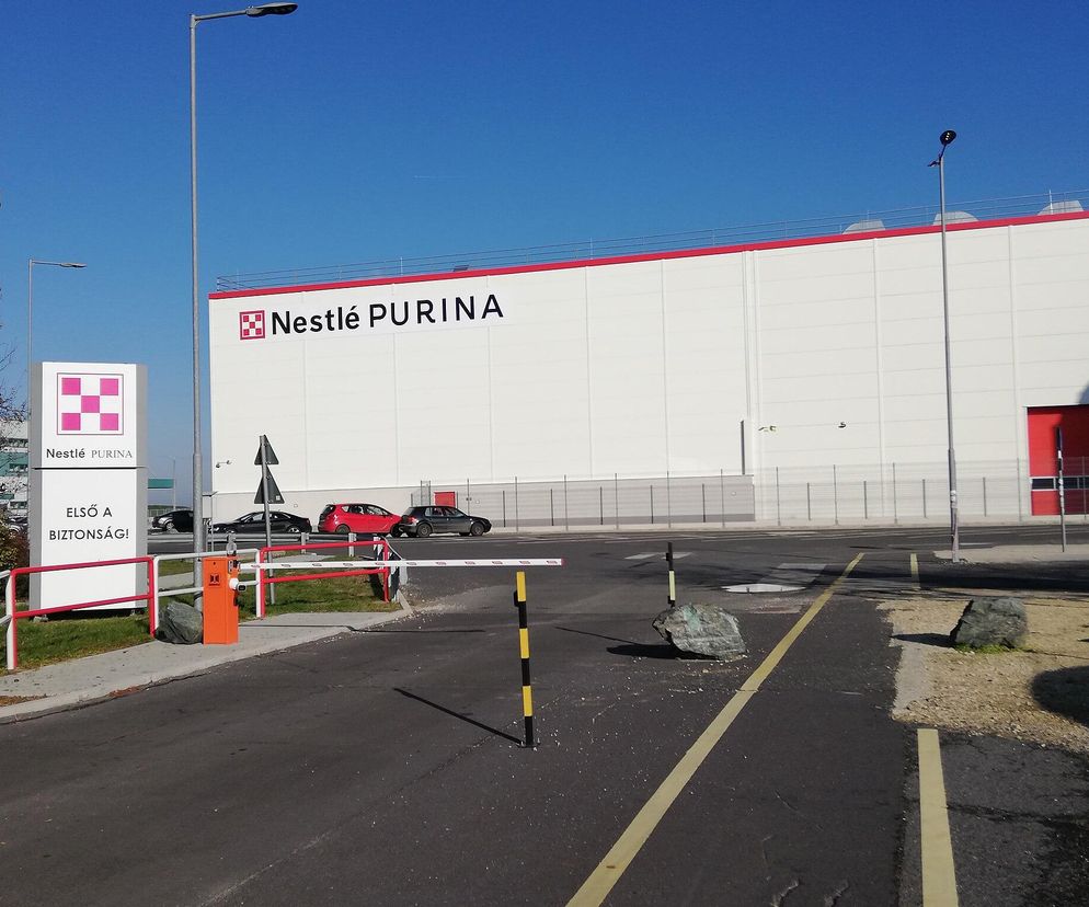 Biała hala produkcyjna Nestle Purina z czerwonymi akcentami, widoczna od strony ulicy z zieloną bramą wjazdową, sygnalizująca nadchodzące zwolnienia grupowe. Szczegóły dotyczące redukcji etatów w globalnym koncernie spożywczym znajdziesz na Super Biznes.