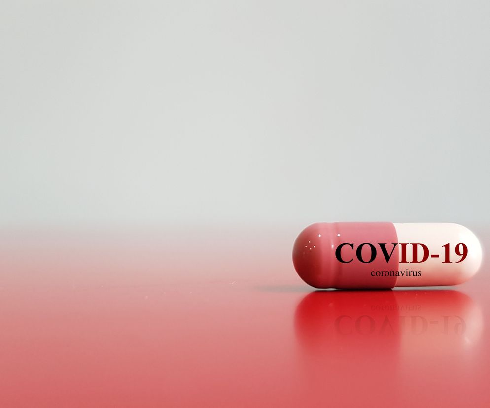 Kapsułka leku z napisem COVID-19 coronavirus na czerwonym blacie, symbolizująca poszukiwania skutecznych terapii. O badaniach nad lekami na koronawirusa można przeczytać na portalu Poradnik Zdrowie.