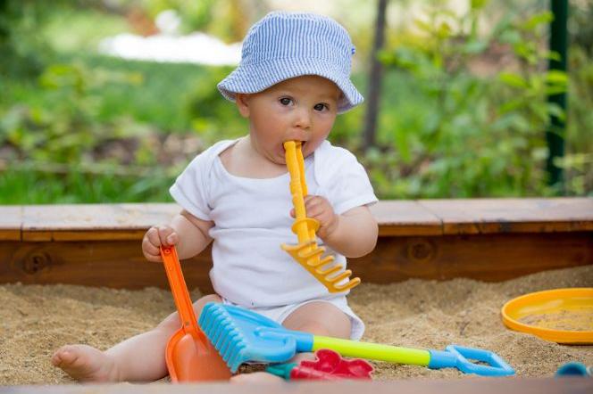 dziecko w piaskownicy wkładające łopatkę do buzi