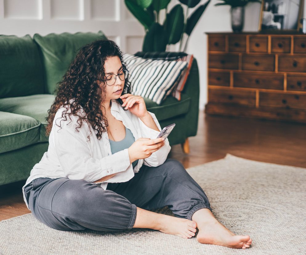 Kobieta plus size siedzi na dywanie z telefonem w ręku