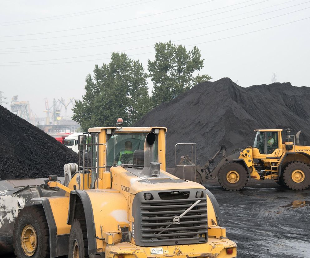 Żółte ładowarki Volvo w składzie węgla, z hałdami opału w tle, symbolizujące rosnące ceny przed sezonem grzewczym. O wyzwaniach związanych z kosztami ogrzewania domów w Polsce przeczytasz więcej na Super Biznes.