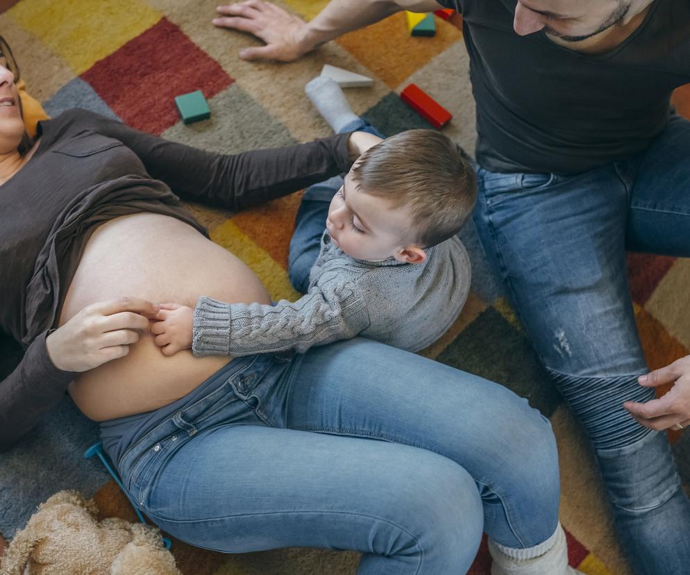 kobieta w ciąży i jej mąż bawią się z dzieckiem na podłodze 