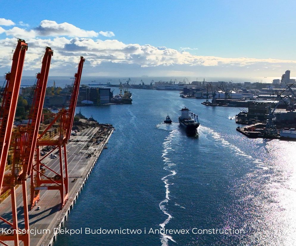 Żurawie portowe w Gdyni, przygotowujące do transportu elementów Polskiej Stacji Antarktycznej im. H. Arctowskiego, co widać na Architektura Murator Plus. Statek z ładunkiem płynie przez port, a w tle panorama Gdyni i morze pod błękitnym niebem.
