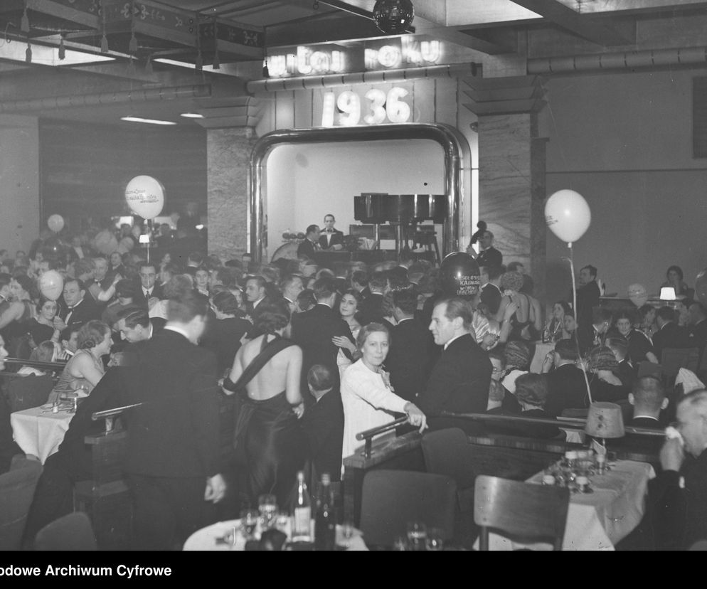 Goście bawiący się na sylwestrowym balu w luksusowym lokalu Adria w Warszawie, z widocznym neonem 1936 i dekoracyjnymi balonami. Eleganckie wnętrze i tłumy świadczą o popularności miejsca, o którym można przeczytać na portalu Architektura Murator Plus.